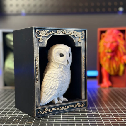 White owl figurine in a decorative black frame on a grid surface.